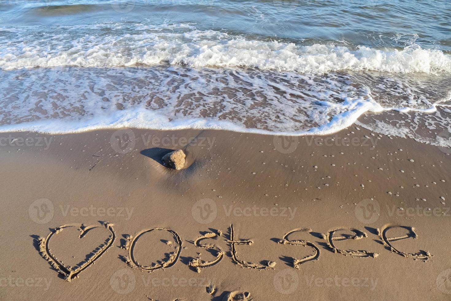 la palabra alemana ostsee mar báltico y un corazón escrito en la arena de la playa. foto