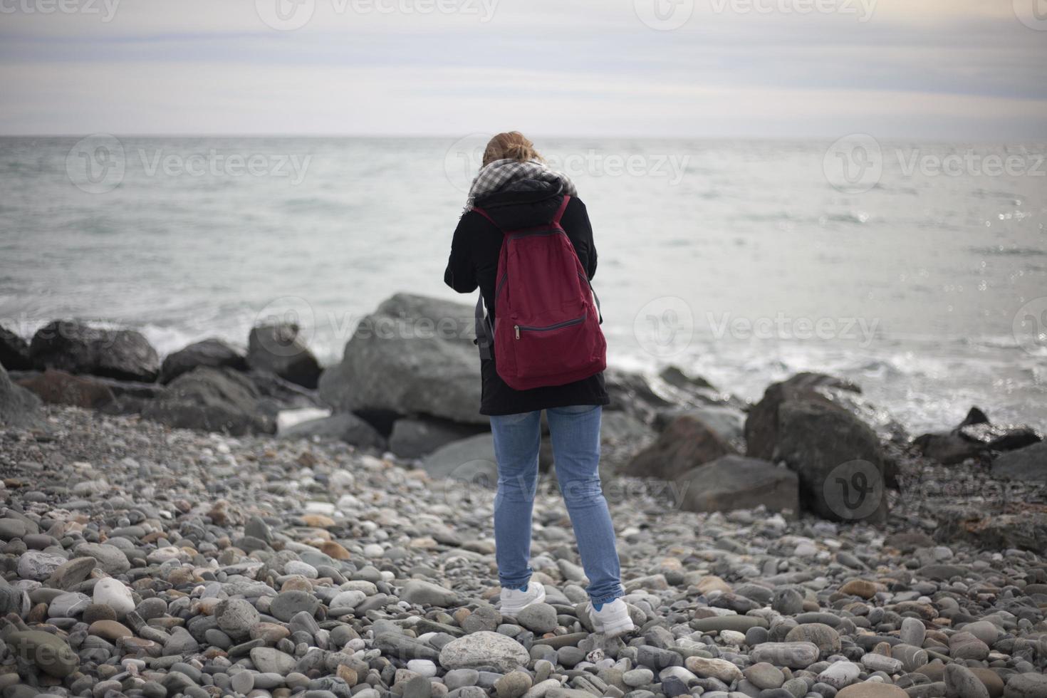 Girl takes pictures of seashore. Woman photographer. Search for story for frame. Big stones. Rocky beach. photo