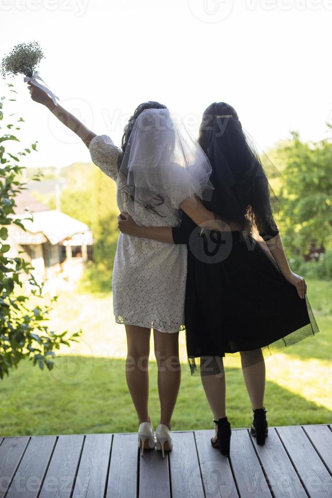 Bride in white dress with friend. Girl with bouquet of flowers in summer. Wedding details. photo