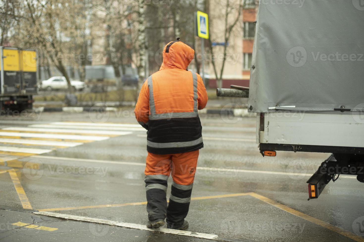 Worker puts cargo in transport. Orange clothes for work. Cleaning road. photo