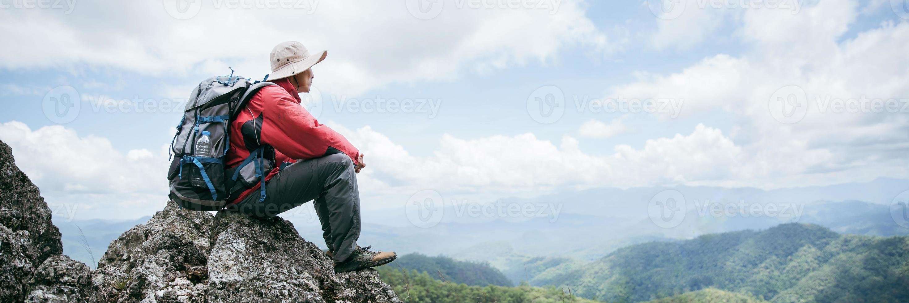 Young person hiking male on top rock, Backpack man looking at beautiful mountain valley at sunlight in summer, Landscape with sport man, high hills, forest, sky. Travel and tourism. photo