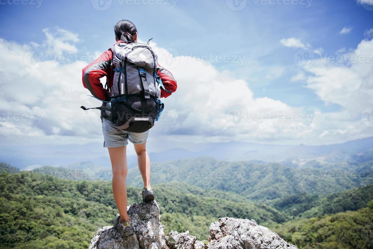 Young person hiking female standing on top rock, Backpack woman looking at beautiful mountain valley at sunlight in summer, Landscape with sport girl, high hills, forest, sky. Travel and tourism. photo