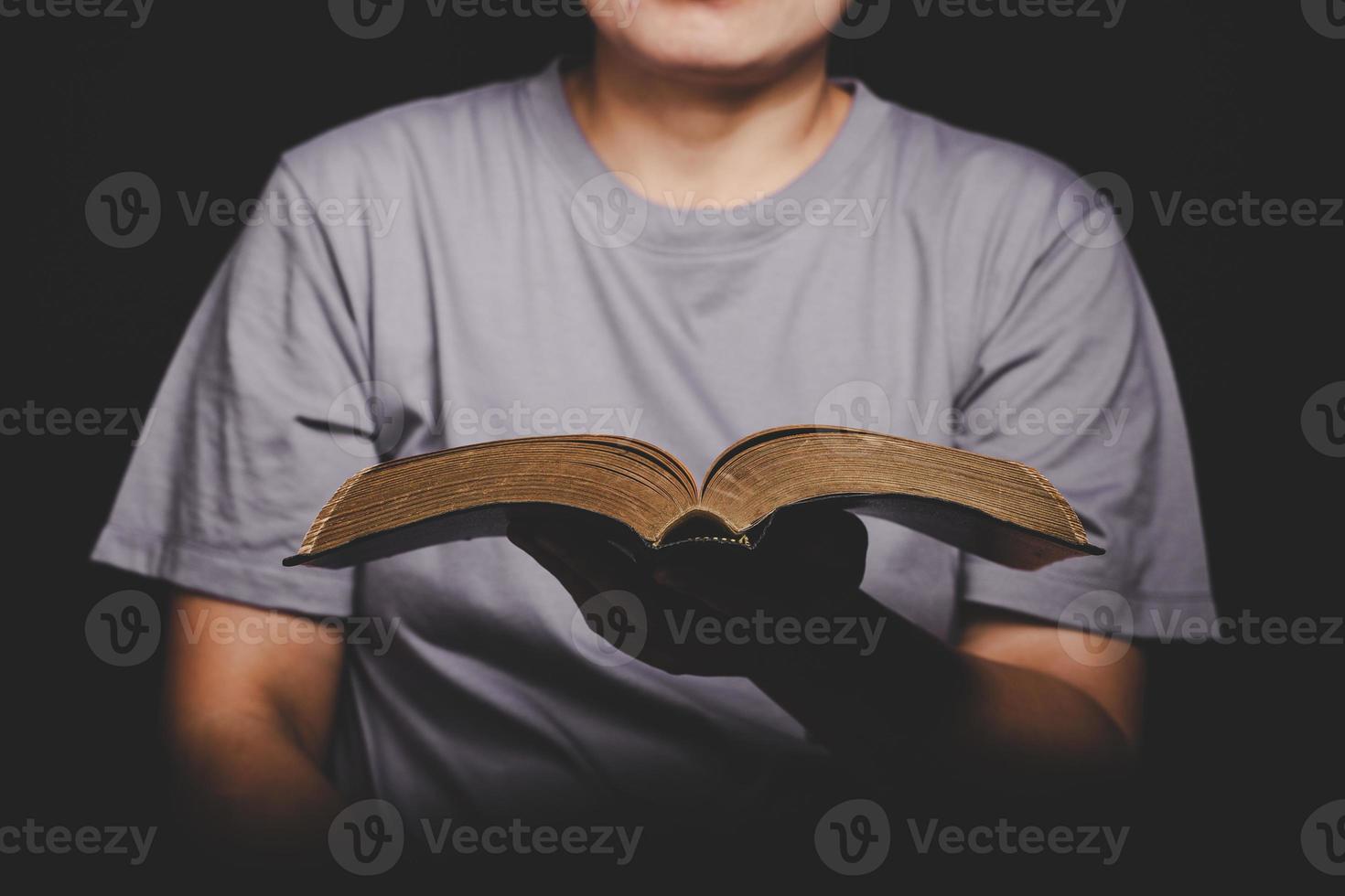 Close up of christian woman hand holding holy bible pray and worship for thank god in church with black background, adult female person are reading book, photo