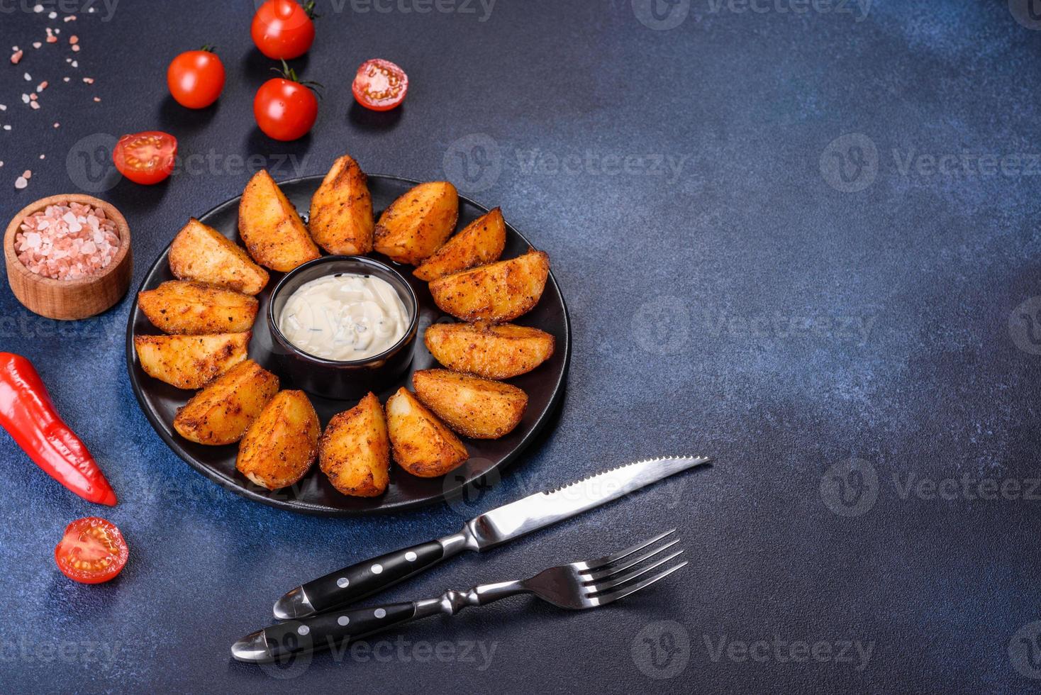 Baked potato wedges with cheese and herbs and tomato sauce on a dark background photo