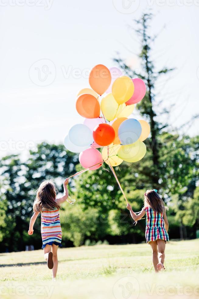 Two little girls holding a bunch of balloons together. photo