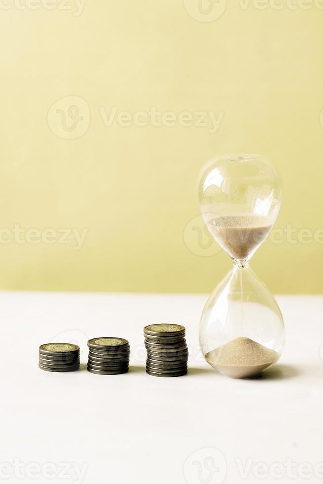 hourglass and stack of coins on table, photo