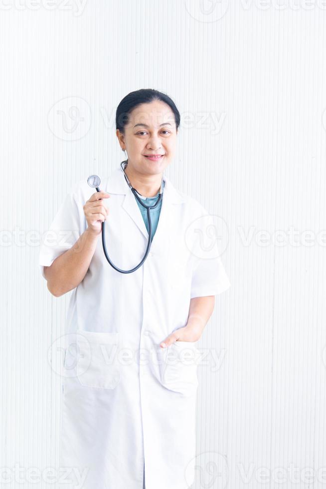 retrata a una doctora sonriente y segura de sí misma con uniforme blanco con el dispositivo médico estetoscopio en el suelo negro blanco en el hospital. doctora asiática en bata médica negocio de atención médica foto