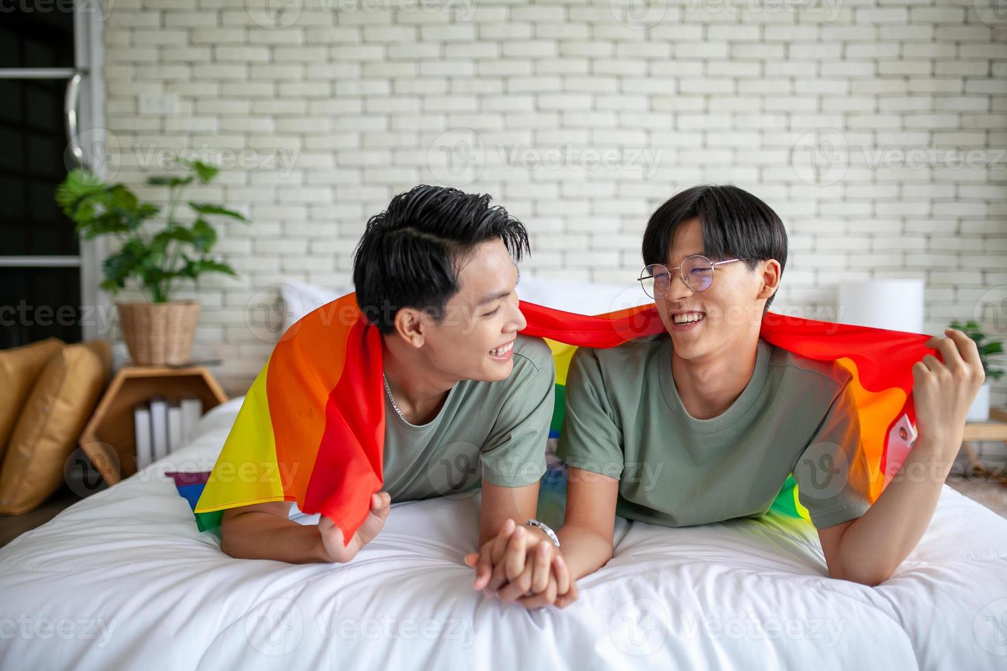Happy asian gay couple holding hands together relaxing at home on bed, LGBTQ concept. photo