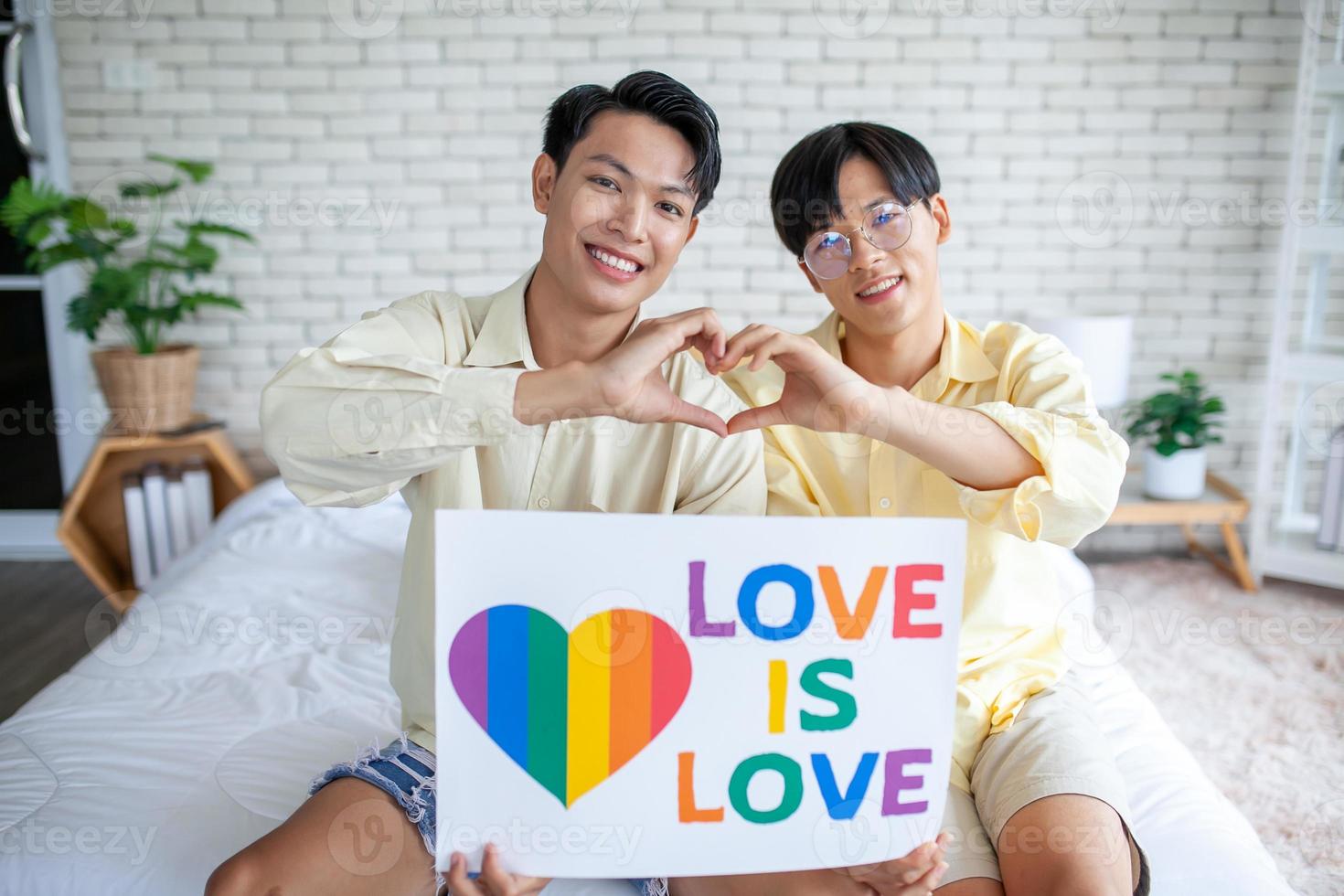 pareja gay asiática con cartel de arco iris lgbt en casa, concepto lgbtq. foto