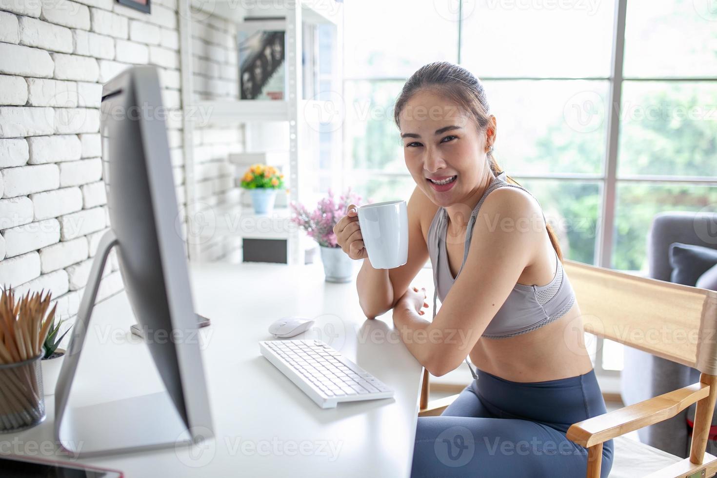 Young Asian woman using laptop computer checking social media application on website online with coffee at home, feel relax and enjoy communicate and discuss  in living room. photo