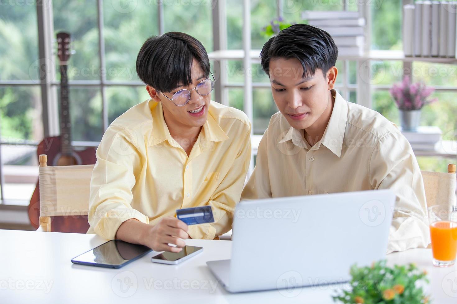 Asian gay couples are using laptop or shopping online with credit card,  LGBTQ concept. photo