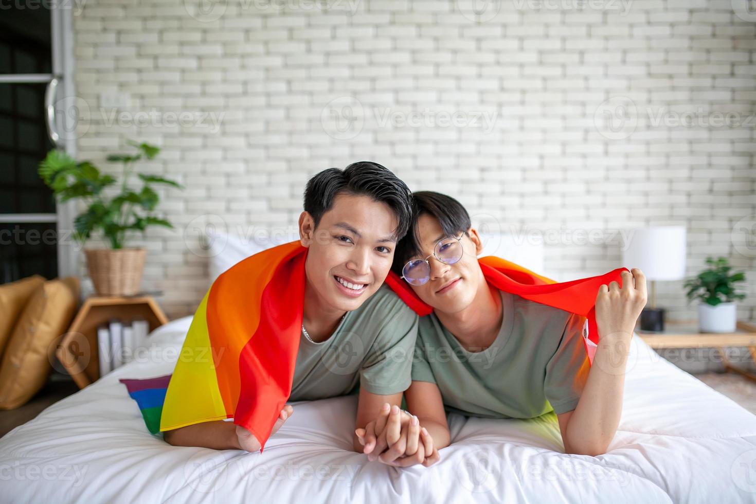 Happy asian gay couple holding hands together relaxing at home on bed, LGBTQ concept. photo