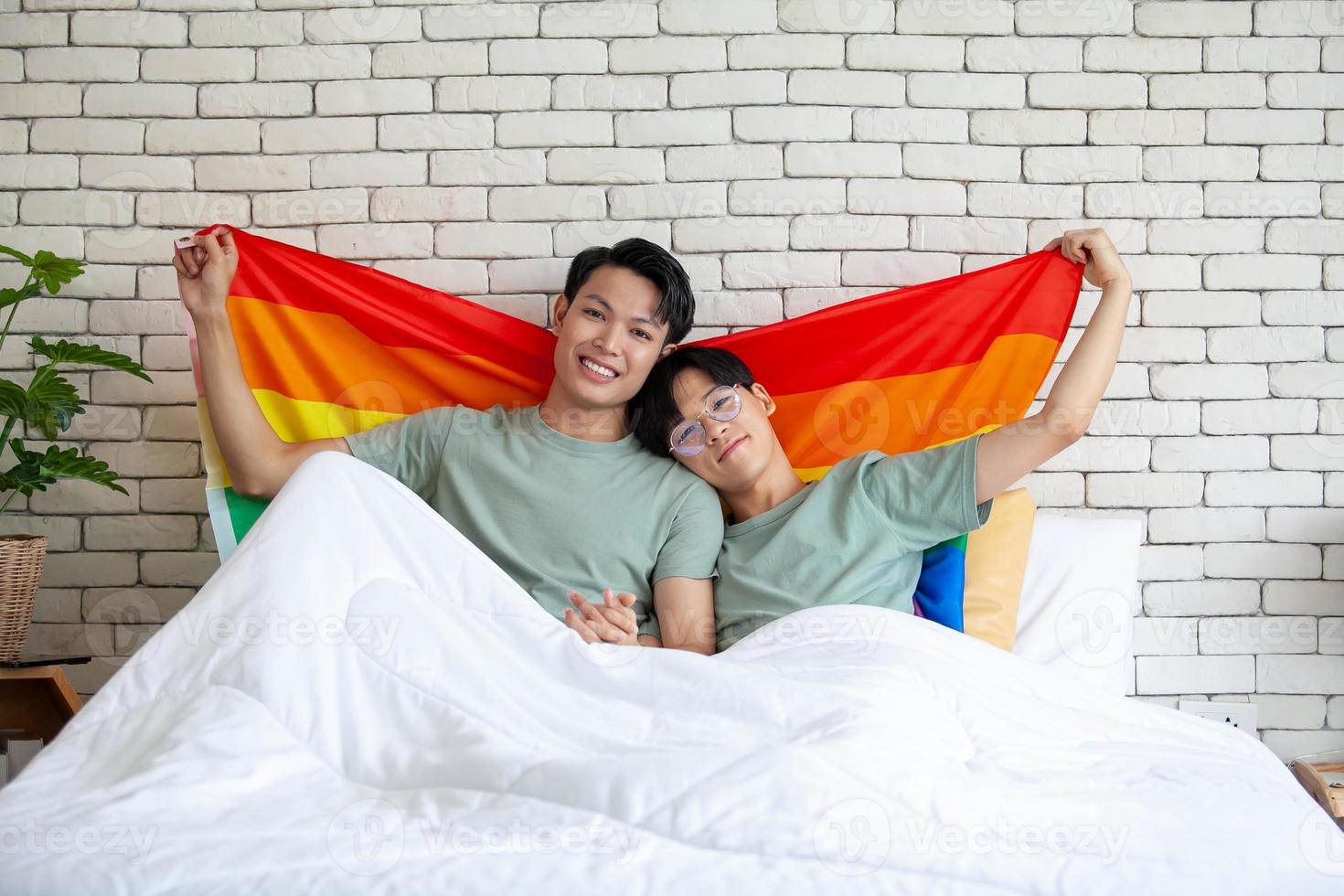 Happy asian gay couple talking together and relaxing at home on bed, LGBTQ concept. photo