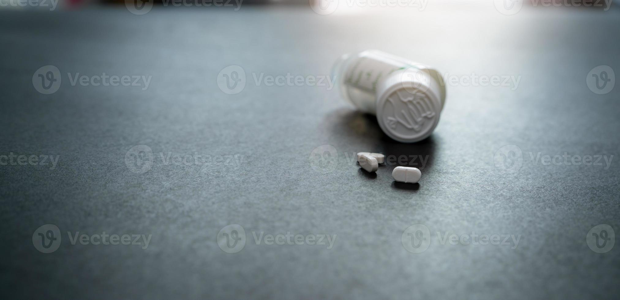 White tablets pills and blur child-resistant pill bottle on black table. Prescription drugs. Pharmaceutical industry. Medical care. Medication for cure illness. Pharmacy product. Small white tablets. photo