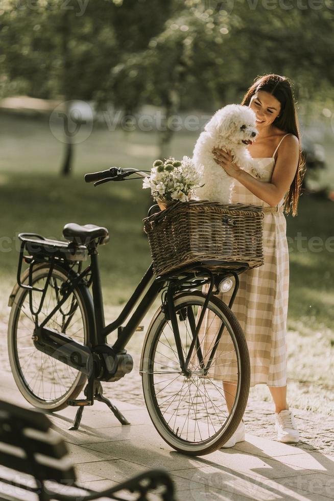 mujer joven con perro bichon frise blanco en la cesta de la bicicleta eléctrica foto