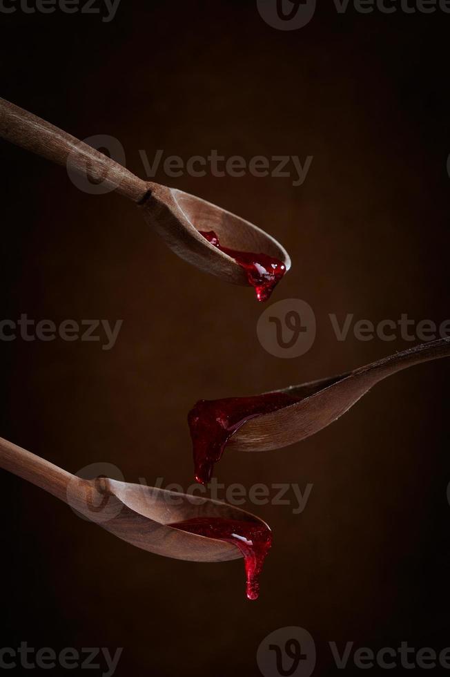 Fruit red jam dripping from spoon to spoon on brown background. photo