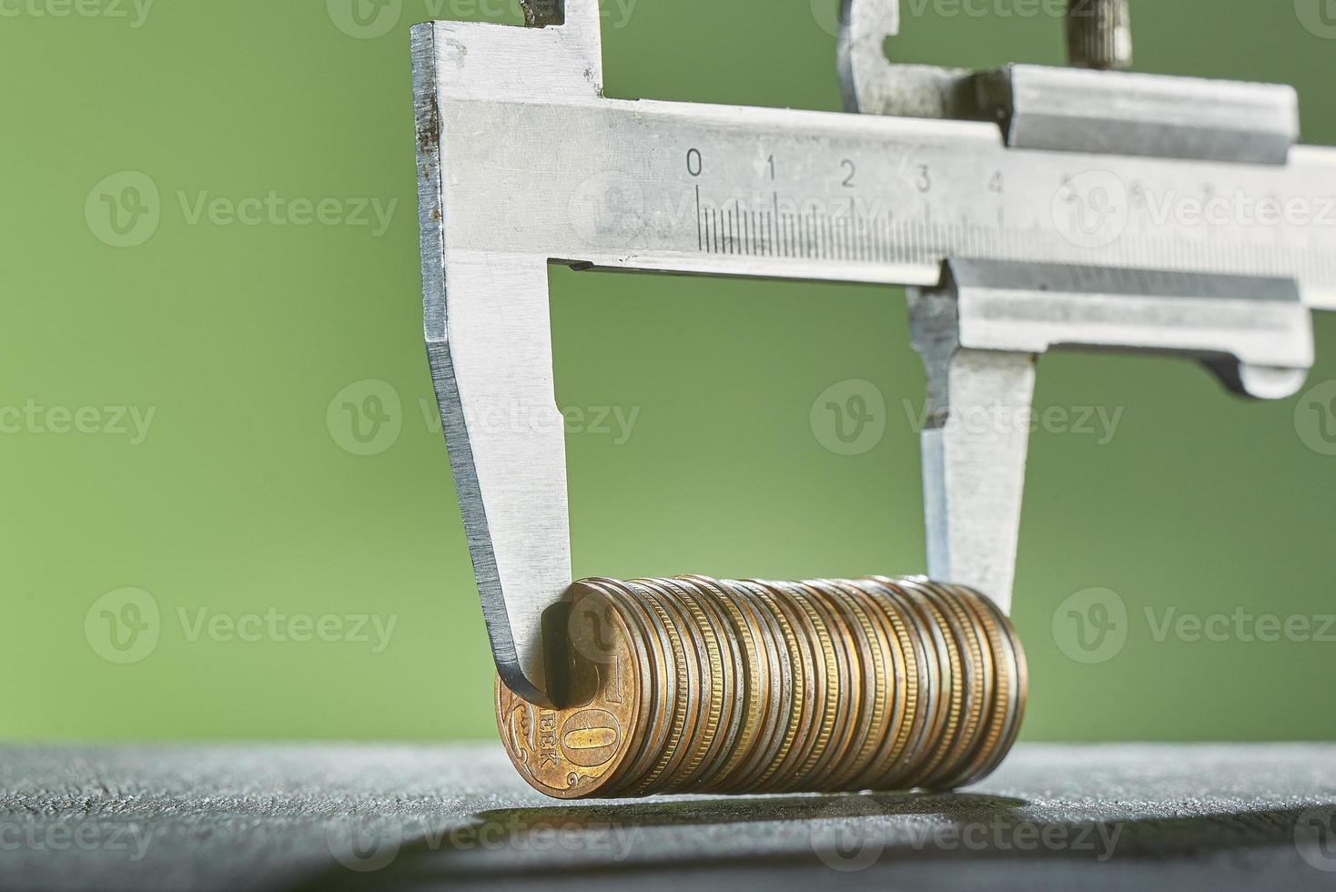 Calipers and stack of coins close-up against a green wall. photo