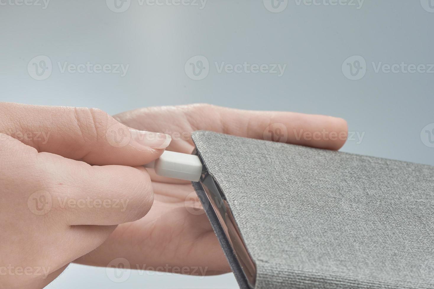 Girl's hands close-up connect the charging cable to the tablet on gray background. photo