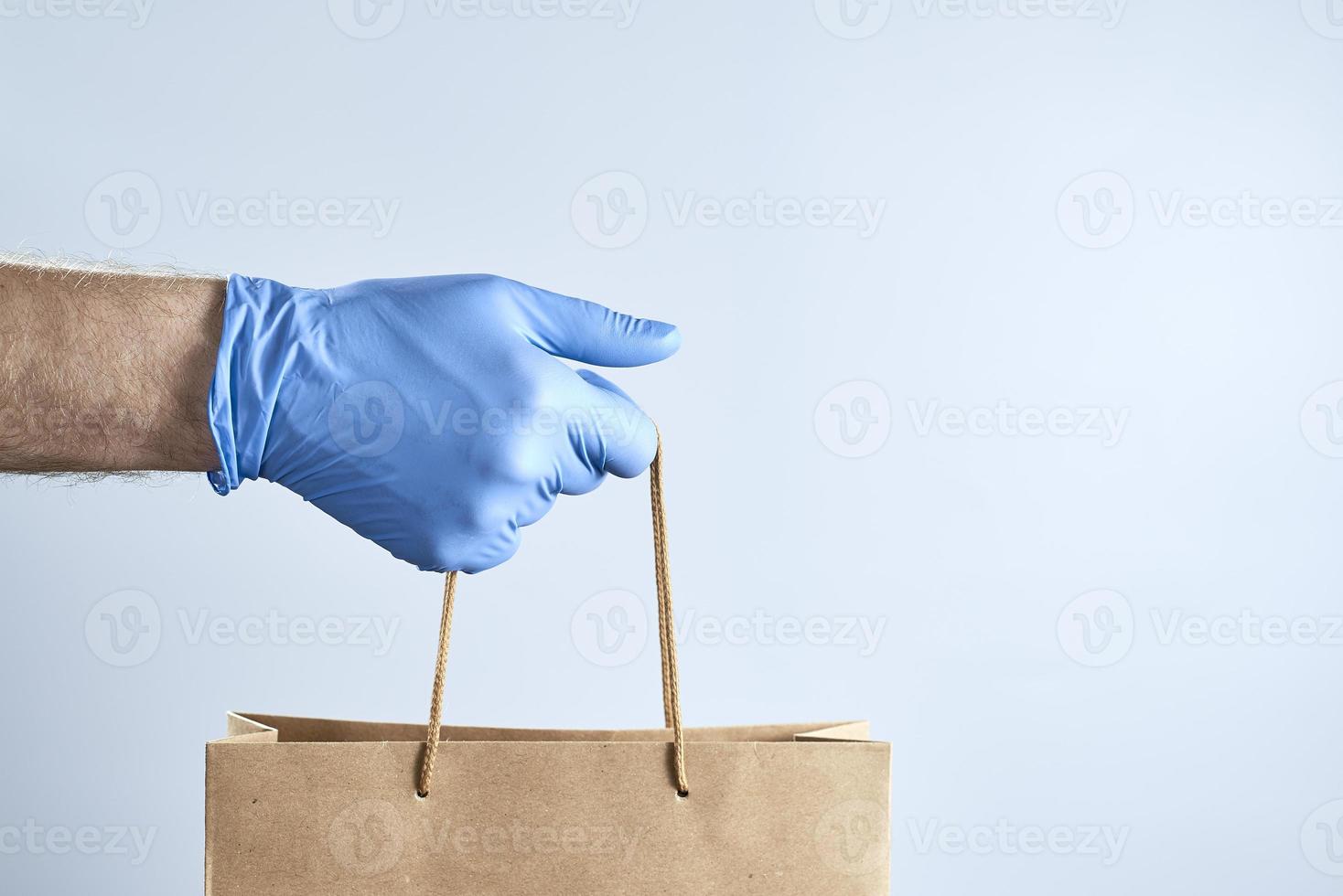 Hand in blue rubber gloves holds a paper bag. Photo with copy space. Concept of security during a pandemic.