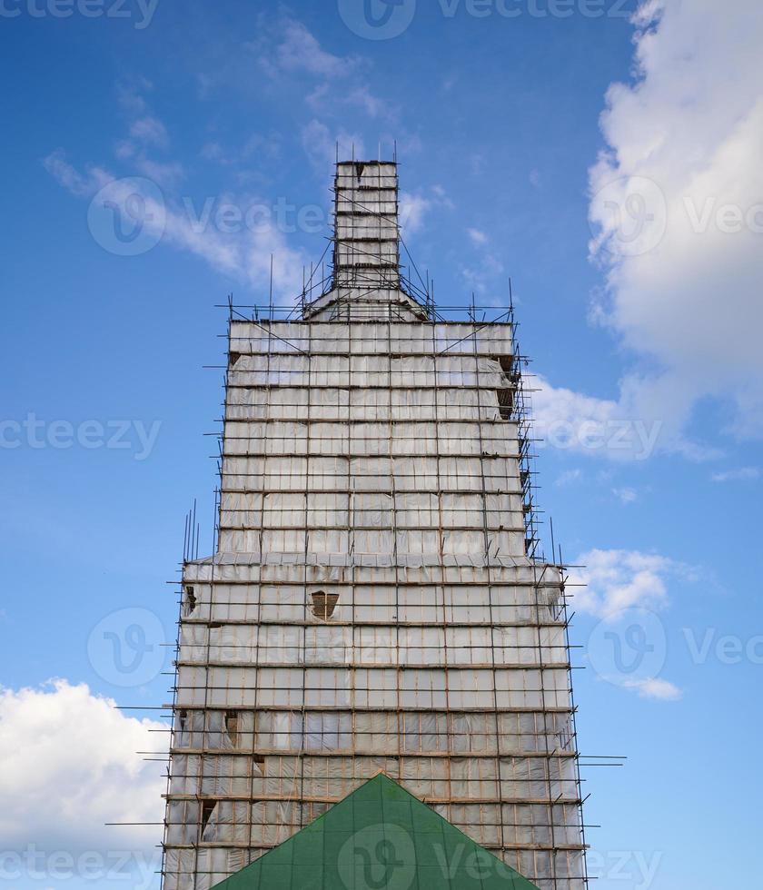 Scaffolding from planks around old bell tower. Background blue sky with clouds. photo