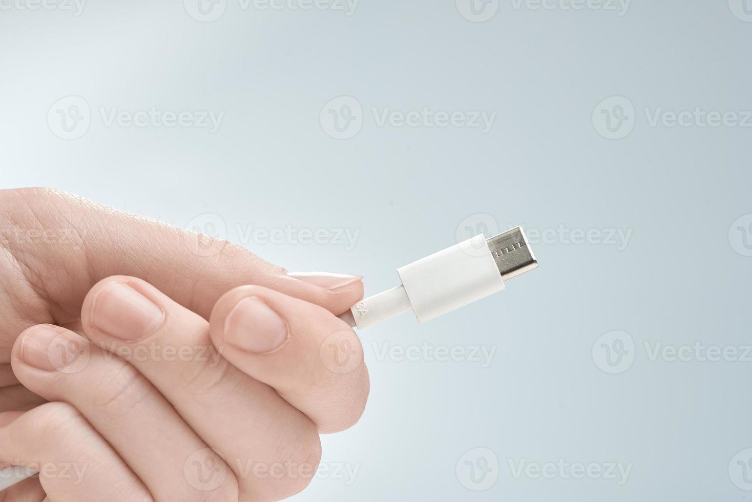 Fingers holding white type-c cable connector on a gray background. photo