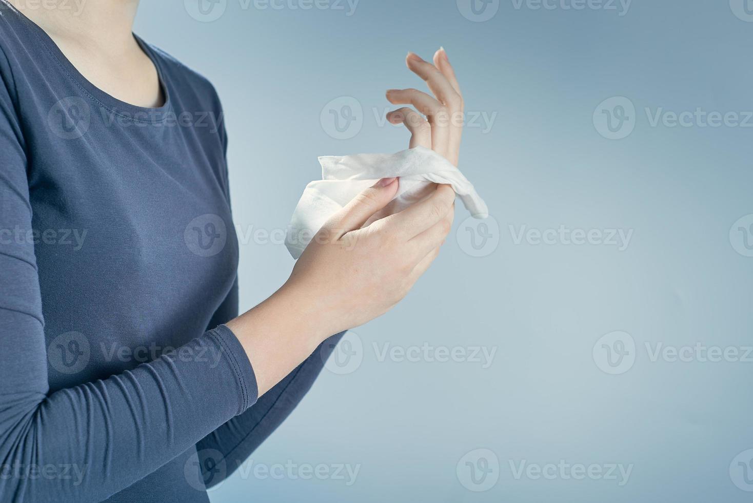 Girl cleaning her hands by using white antibacterial napkin on gray background. Photo with copy space.