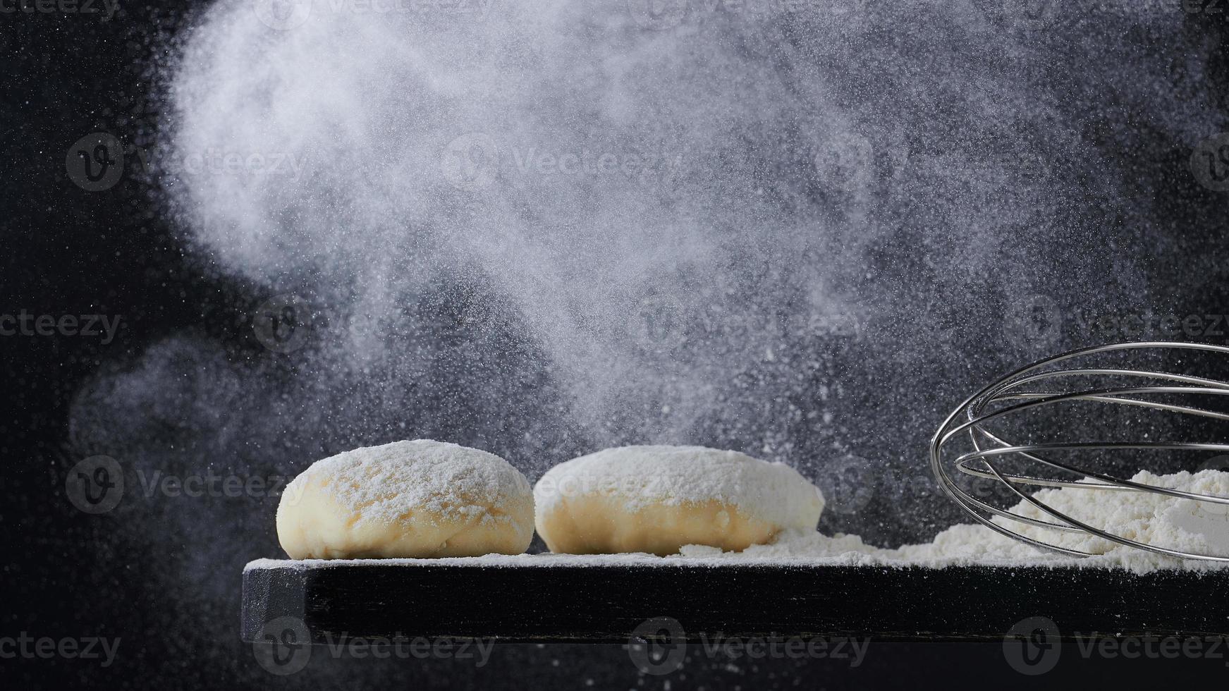 Flour pours on fresh homemade dough. Dough with spilled flour on a black background. Yeast dough for bread, rolls, pizza or pie. Copy space. photo