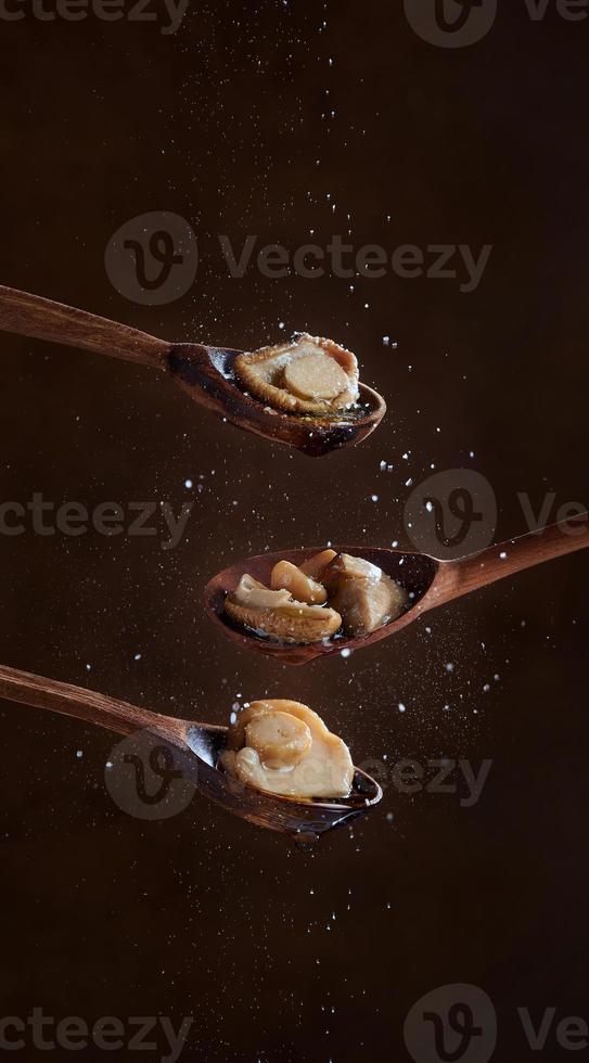 Pickled Boletus mushrooms on wooden spoons on dark background. Salt is poured on the mushrooms. The concept of homemade preparations. photo