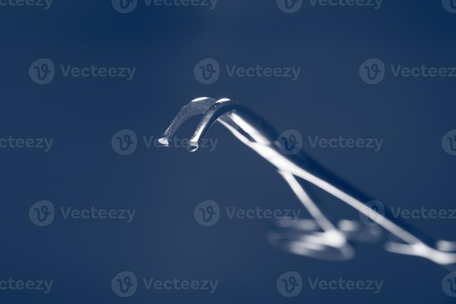 Surgical clip in soft focus on a blue background. The handle of the medical instrument in the blur. photo