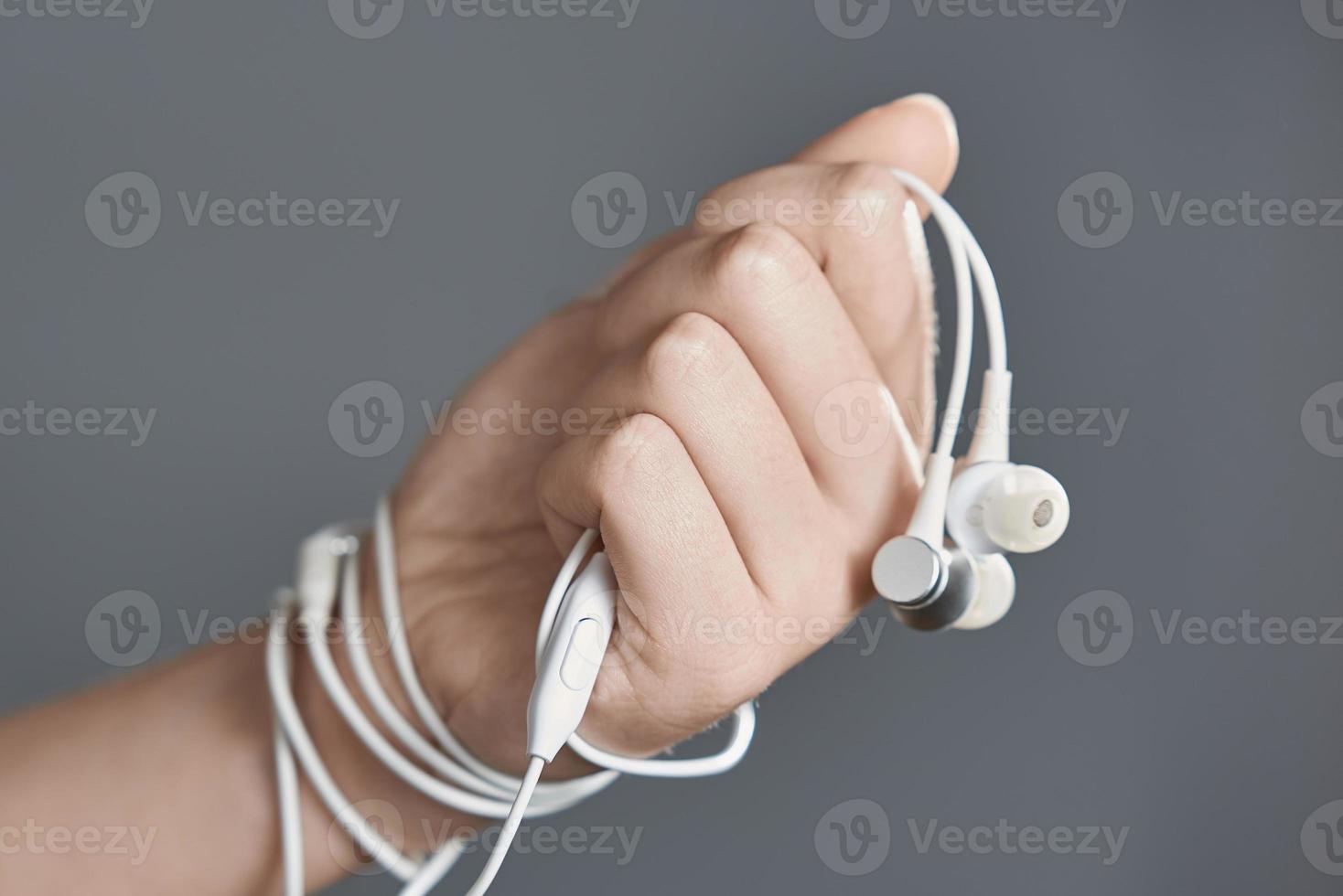 White headphones in his fist. The wire binds the hand. The concept of dependence on headphones. photo