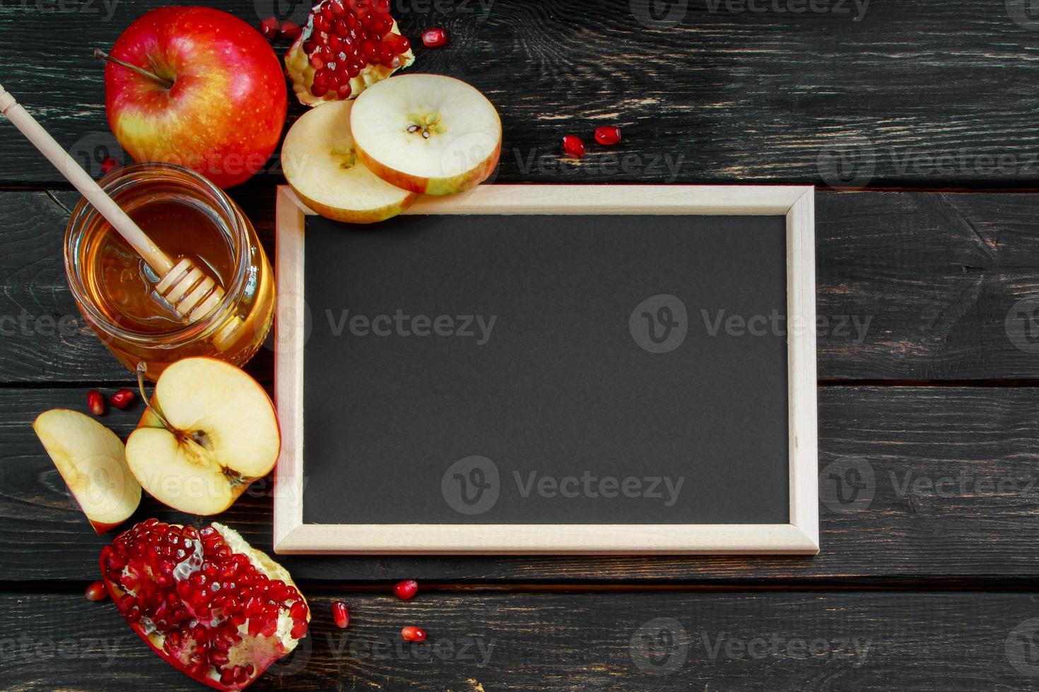 Rosh Hashanah celebration. Honey, apples and pomegranates on dark wooden background. Frame for congratulatory text. Jewish traditional religious holiday. photo