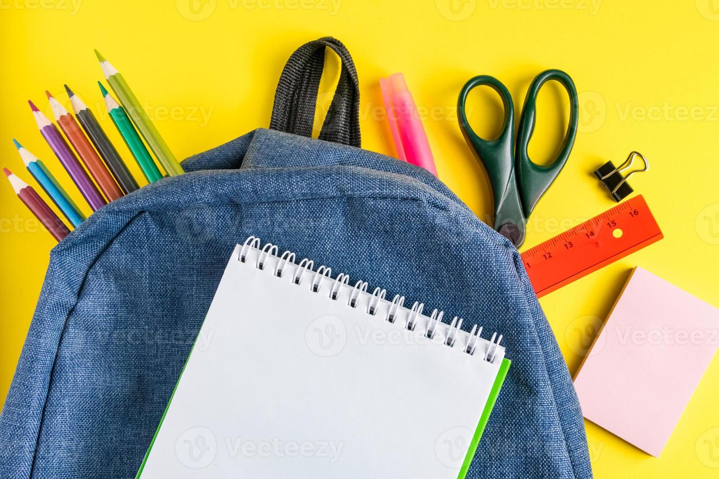 School backpack with office supplies on  yellow background. Place for text. photo