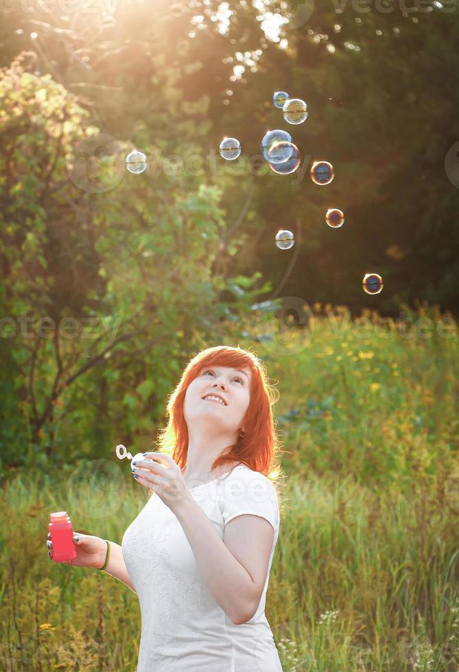 Dreamy young red haired woman with soap bubbles. Happy girl in nature in the sun. A symbol of freedom and enjoyment. photo