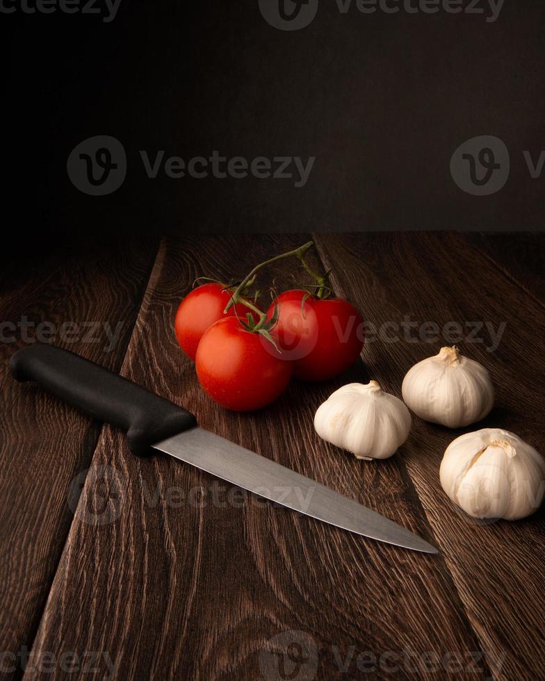 Garlic bulbs, tomatoes and a knife on a dark wood table with copy space above photo