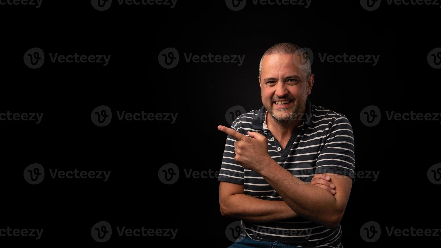 Smiling man pointing on a black background with copy space photo