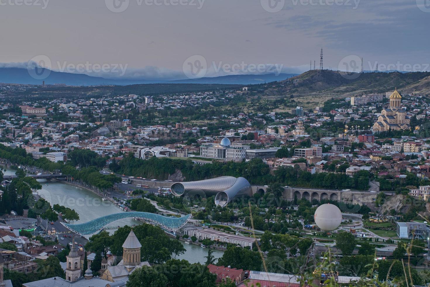 Tbilisi, Georgia sunset Panoramic view from top of fortress of Narikala showing the bridge of peace, Rike Park, Kura River and Holy Trinity Cathedral photo