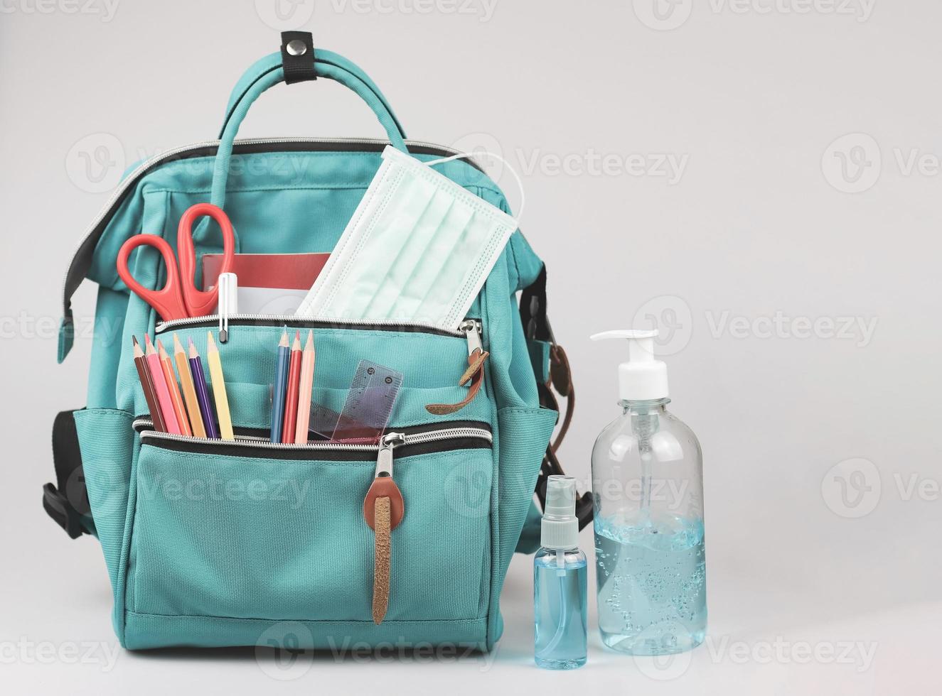 mochila con material escolar, mascarilla médica y gel desinfectante de alcohol sobre fondo blanco con espacio para copiar. prevención de covid-19 al volver a la escuela y nuevo concepto normal. foto