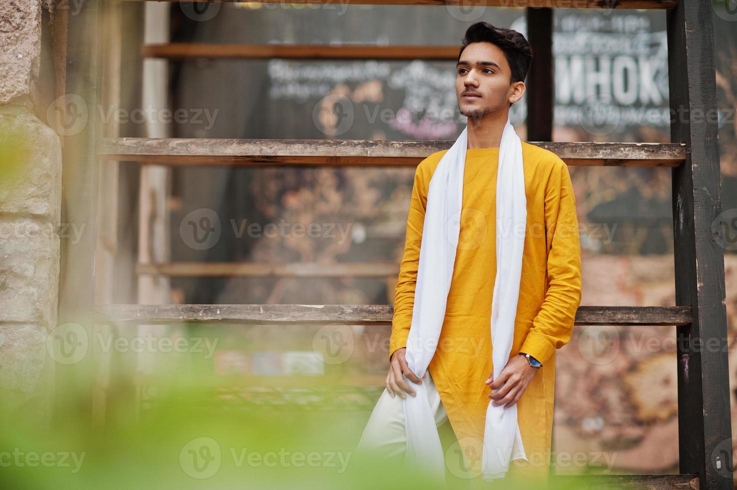 Indian stylish man in yellow traditional clothes with white scarf posed outdoor. photo