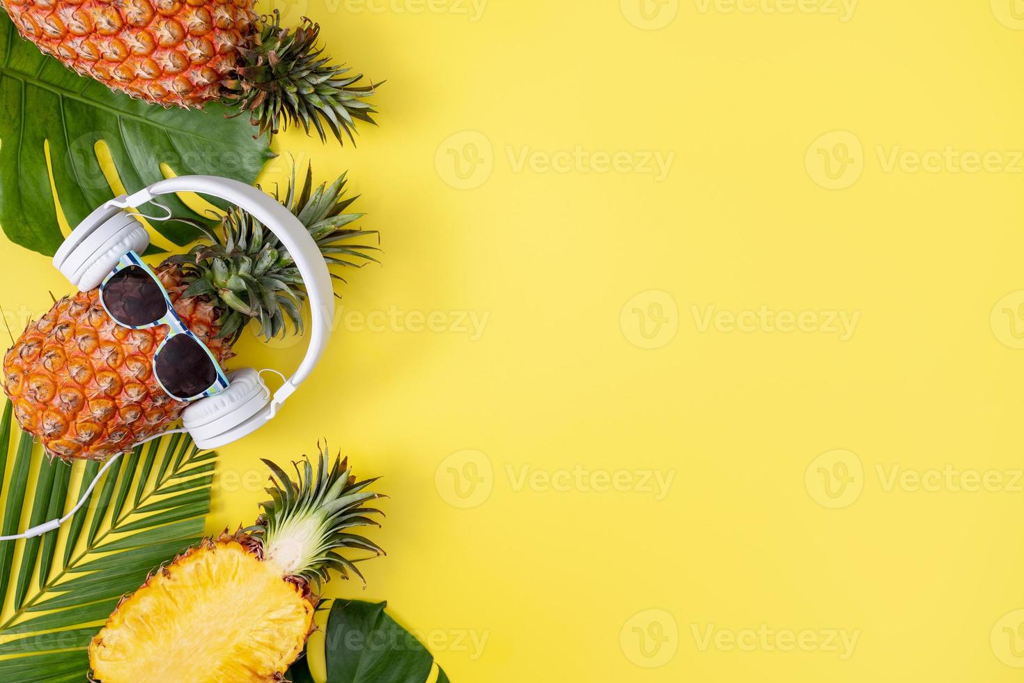 piña divertida con auriculares blancos, escuchar música, aislada en fondo amarillo con hojas de palma tropical, vista superior, concepto de diseño plano. foto