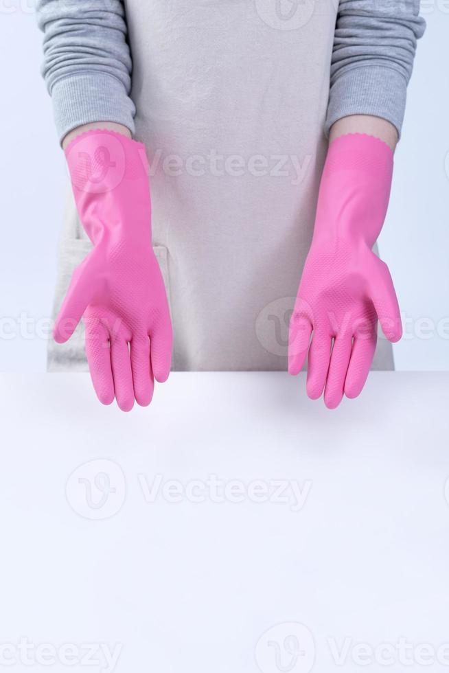 Young woman housekeeper in apron is wearing pink gloves to clean the table, concept of preventing virus infection, housekeeping service, close up. photo