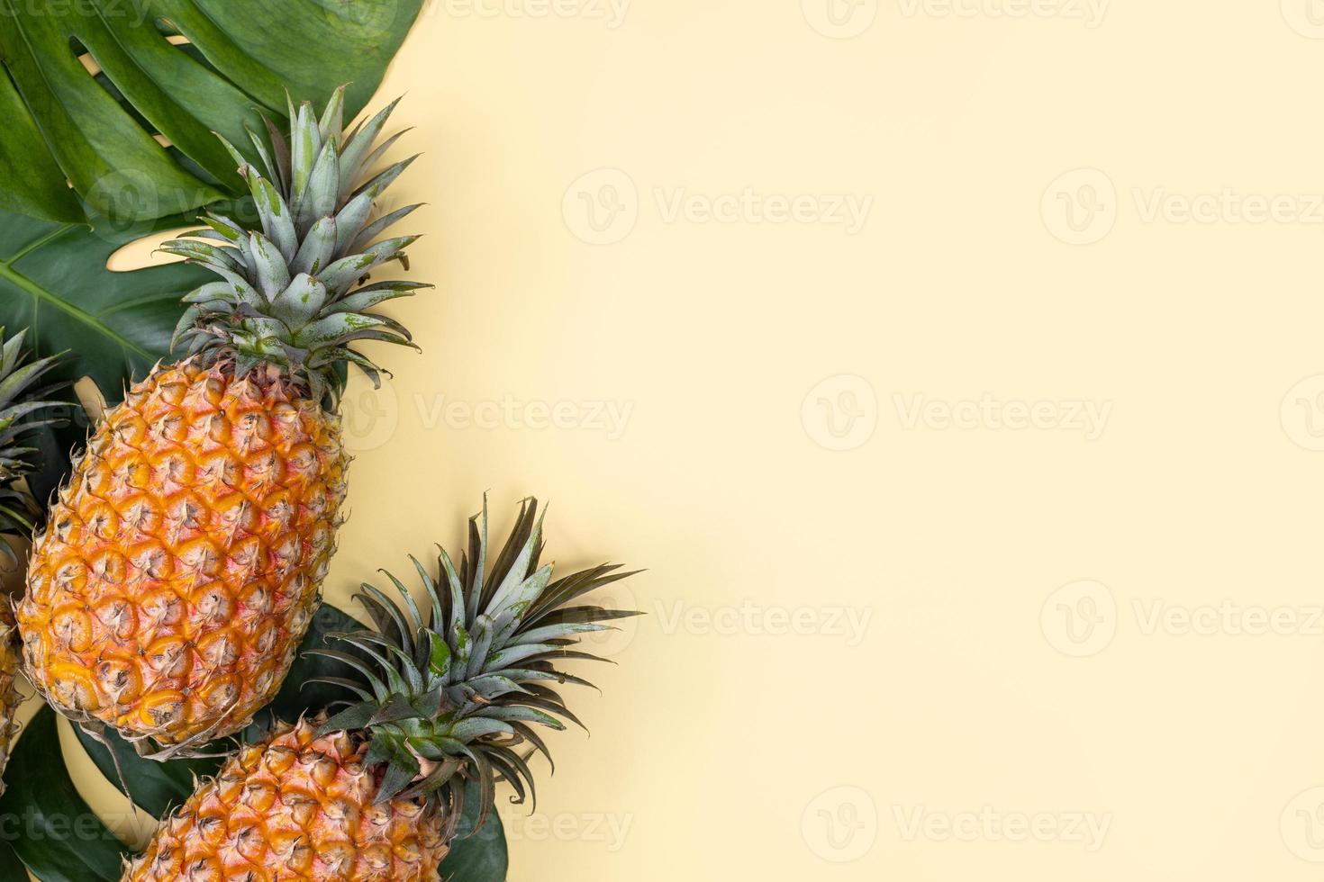 Beautiful pineapple on tropical palm monstera leaves isolated on bright pastel yellow background, top view, flat lay, overhead above summer fruit. photo