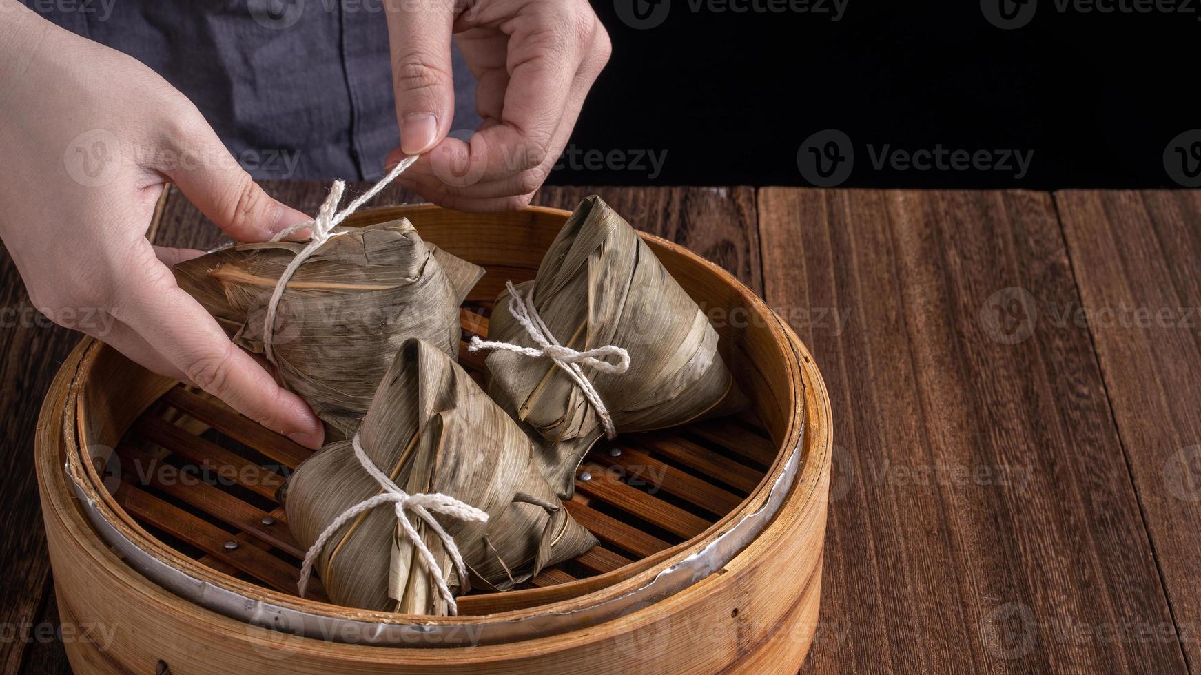 Rice dumpling, zongzi - Dragon Boat Festival, Bunch of Chinese traditional cooked food in steamer on wooden table over black background, close up, copy space photo