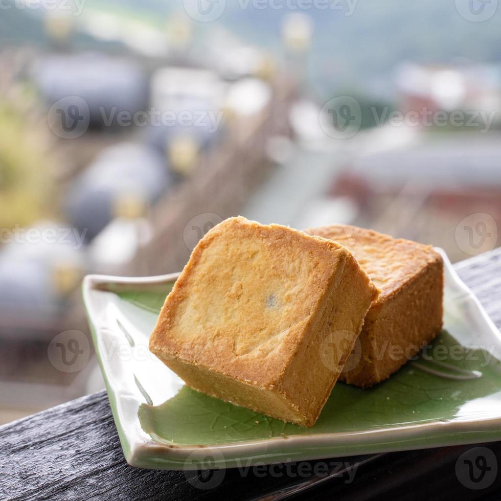 Delicious pineapple pastry in a plate for afternoon tea on wooden railing of a teahouse in Taiwan with beautiful landscape in background, close up. photo