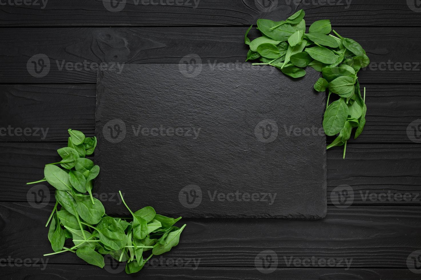 Kitchen table with stone cutting board, decorated with herbs. Presented on the black wooden background with center empty space. Table top view. photo