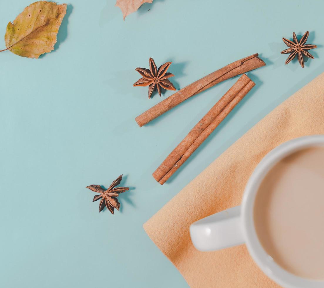 composición de otoño. taza de café, hojas de otoño, palitos de canela y estrellas de anís sobre fondo azul pastel brillante. endecha plana, espacio de copia de vista superior. foto