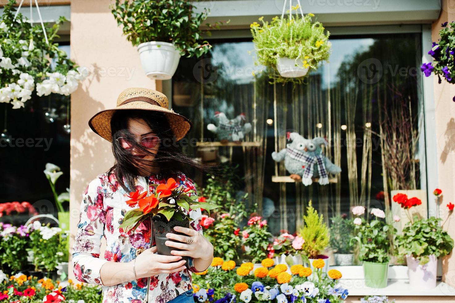 Summer portrait of brunette girl in pink glasses and hat against flowers shop. photo