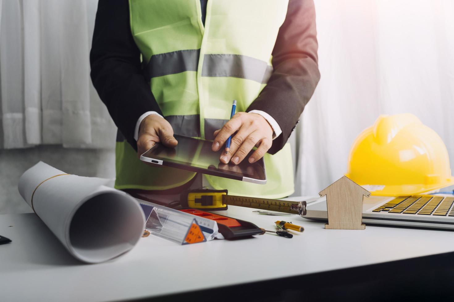 Dos colegas discutiendo el trabajo de datos y una tableta, un portátil con un proyecto arquitectónico en el sitio de construcción en un escritorio en la oficina foto