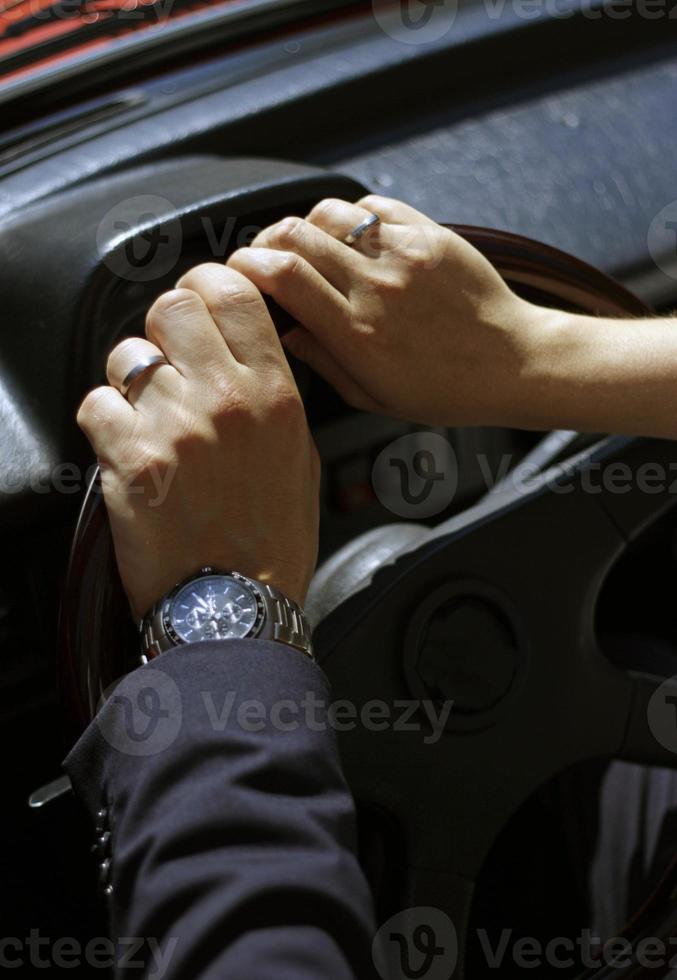 Closeup of newlyweds with hands on the steering wheel, presenting their wedding rings photo