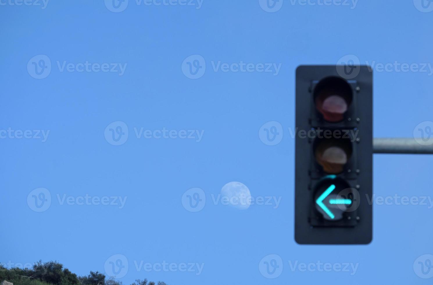 The arrow of a traffic light pointing at the moon with blue sky around it photo