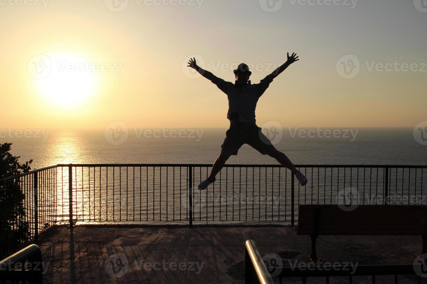 silueta de un hombre saltando cerca de la costa durante la puesta de sol foto